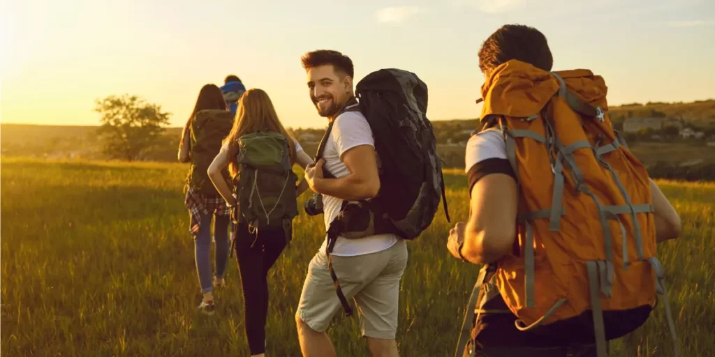 A group of hikers with backpacks walking through a scenic grassy trail at sunset, training for the Camino de Santiago