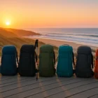 Seven different 30–45 L backpacks lined up on a Portuguese Coastal Camino boardwalk at sunrise, with ocean waves and trekking pole, illustrating 2025 gear comparison.