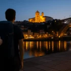 Pilgrim with scallop-shell backpack admiring Porto’s Sé Cathedral and Dom Luís I Bridge at blue-hour dawn on the Douro River.