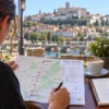 A pilgrim reviewing a Coimbra to Mealhada walking map at an outdoor café table overlooking Coimbra.